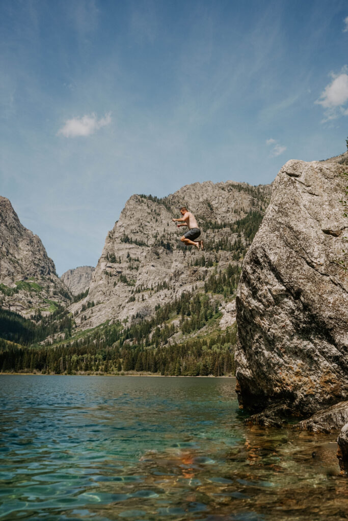 man jumping into blue lake from a big boulder