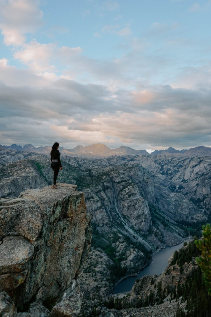 subject on a ledge overlooking a lake and peaks of the Wind River Range